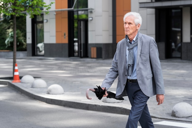Homme plus âgé élégant dans la ville traversant la rue tout en tenant le parapluie
