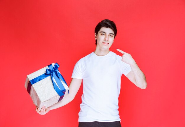 Homme pointant sur sa boîte cadeau blanche avec ruban bleu