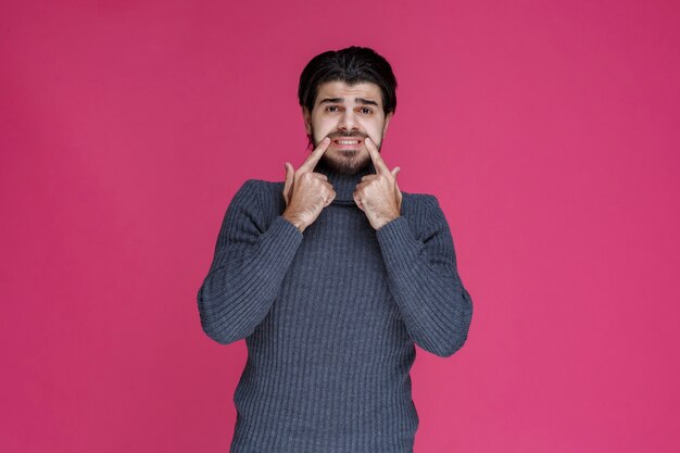 L'homme pointant sa bouche avec les doigts et demande en souriant.