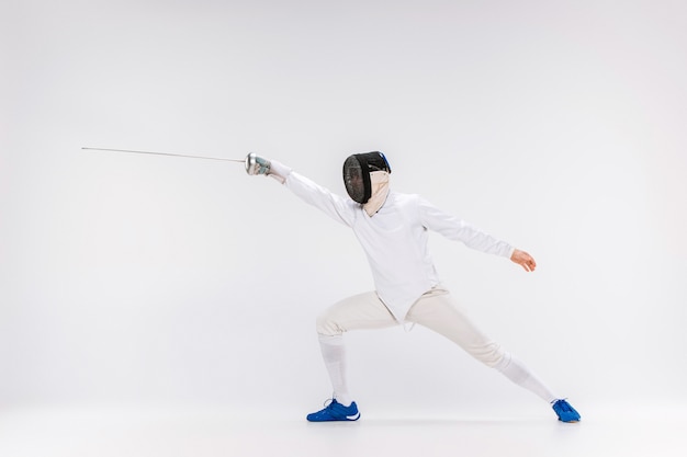 Homme portant un costume d'escrime pratiquant avec l'épée contre le gris