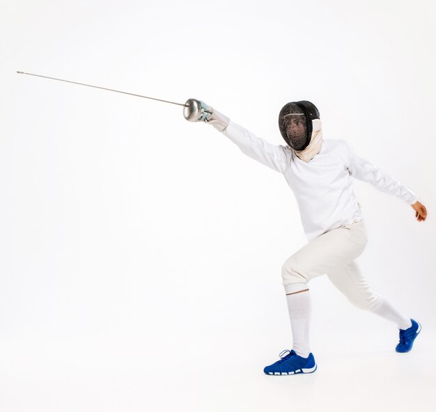 Homme portant un costume d'escrime pratiquant avec l'épée contre le gris