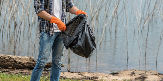 Photo gratuite un homme portant des gants orange ramassant les ordures dans un sac noir.