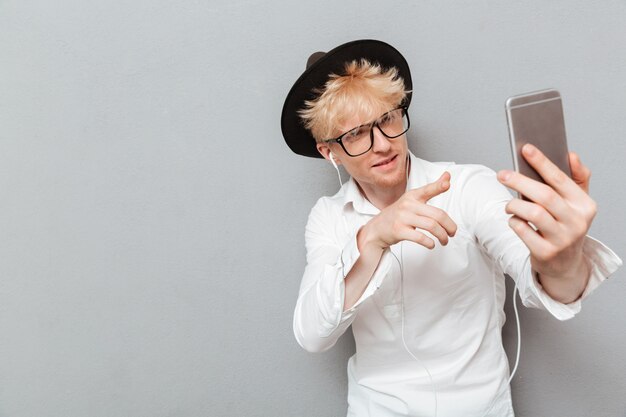 Homme portant des lunettes, écouter de la musique tout en faisant selfie.