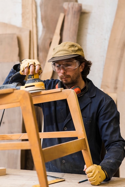 Homme portant des lunettes de sécurité travaillant avec des ponceuses orbitales sur des meubles en bois