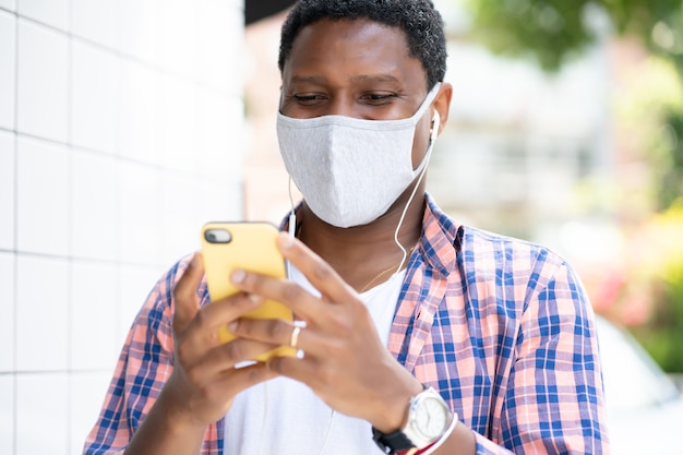 Homme portant un masque facial et utilisant son téléphone portable tout en se tenant à l'extérieur. Nouveau concept de mode de vie normal.