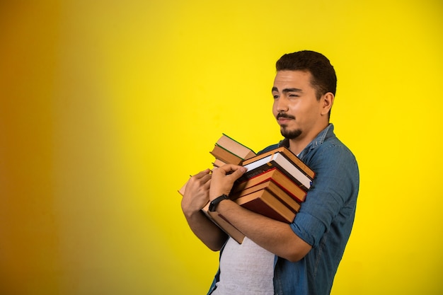 Photo gratuite homme portant une pile de livres lourds à deux mains et à la fierté.