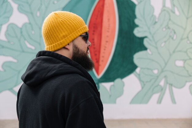 Homme, porter, lunettes soleil, et, tricoter, chapeau, debout, devant, mur peint