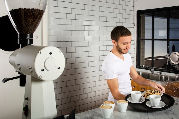 Homme posant sur le plateau des tasses de café et des biscuits