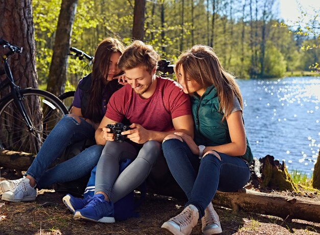 Homme positif et deux filles utilisant un appareil photo numérique compact sur la côte sauvage de la rivière après une balade à vélo.