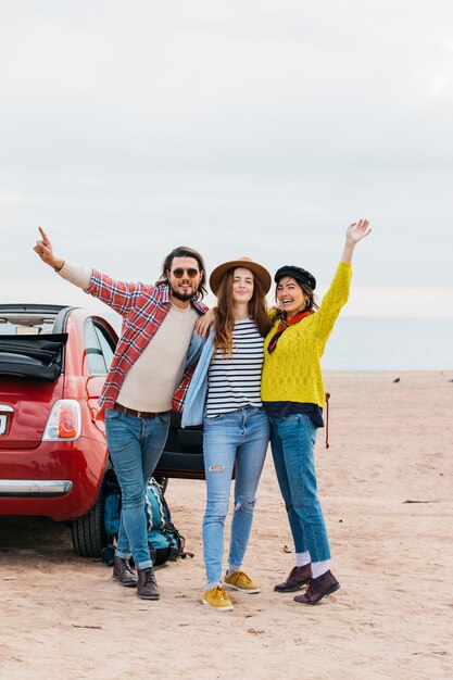 Homme positif et femmes gaies embrassant près d&#39;une voiture sur la côte de la mer