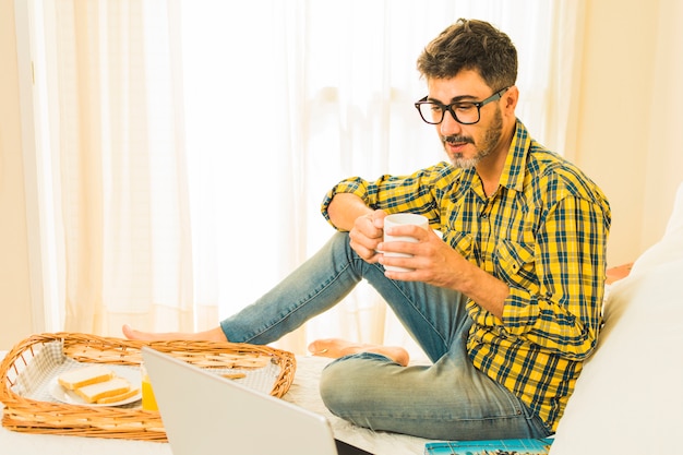 Homme Prenant Son Petit Déjeuner Sur Le Lit En Regardant Un Ordinateur Portable Dans La Chambre