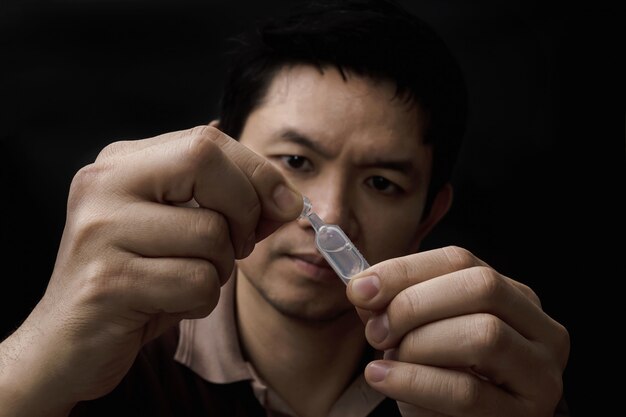 Homme préparant la médecine des gouttes pour les yeux guérir sa douleur aux yeux avec fond noir