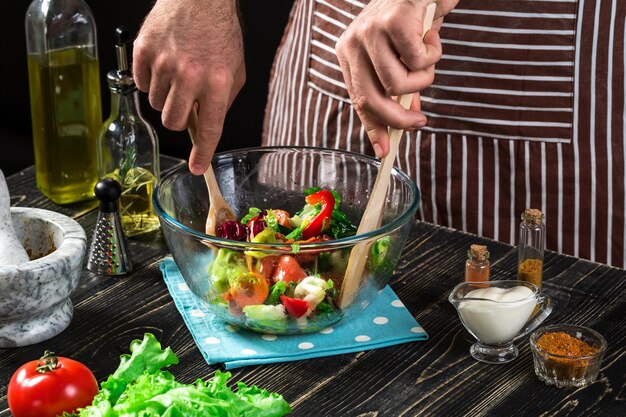 Homme préparant une salade avec des légumes frais sur une table en bois. Cuisiner des aliments savoureux et sains. Sur fond noir. Nourriture végétarienne, concept sain ou de cuisine.