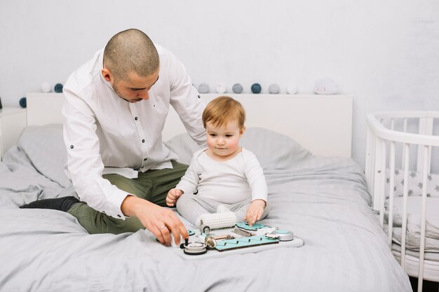 Homme près de petit bébé jouant avec des jouets sur le lit