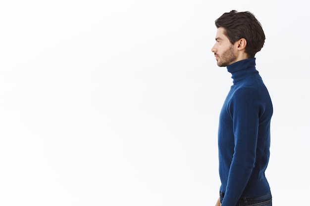 Photo gratuite homme en pull bleu à col haut, debout droit avec une expression déterminée et affirmée, pose un fond blanc sans émotion