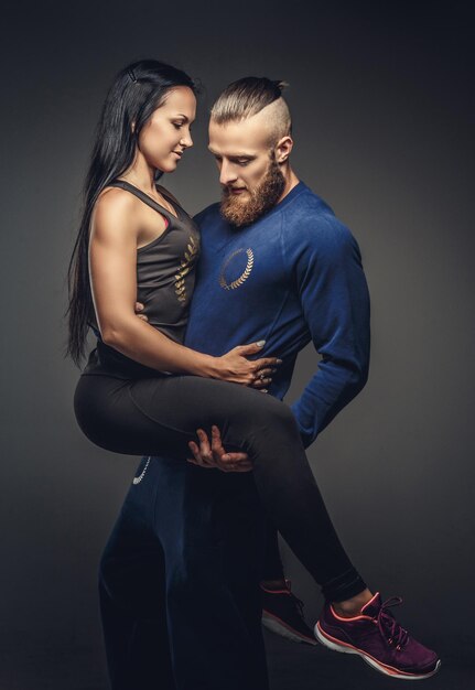 Homme en pull bleu tenant sur les bras femme en vêtements de sport. Isolé sur fond gris.