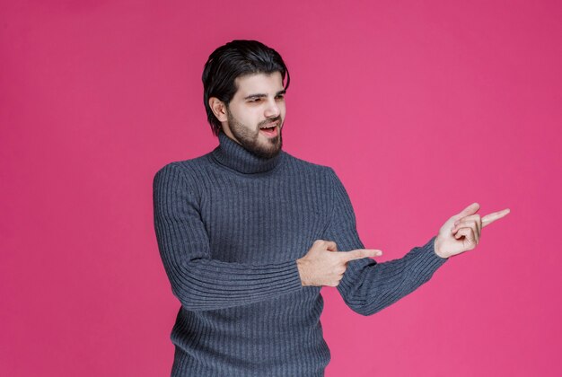 Homme en pull gris pour pointer quelque chose ou présenter quelqu'un à l'aide du doigt pointé.