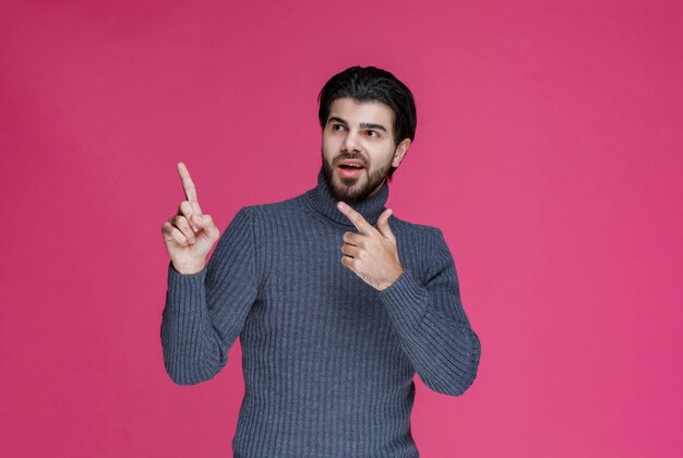 Homme en pull gris pour pointer quelque chose ou présenter quelqu'un à l'aide du doigt pointé.