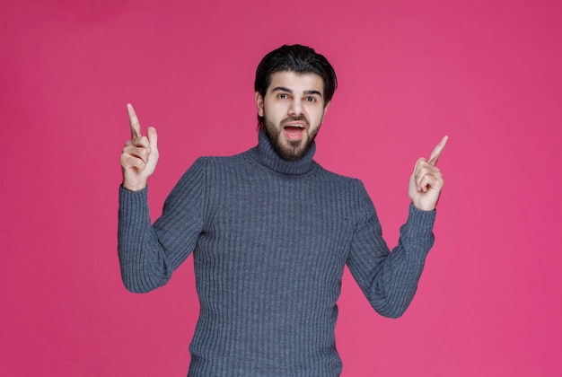 Homme en pull gris pour pointer quelque chose ou présenter quelqu'un à l'aide du doigt pointé.