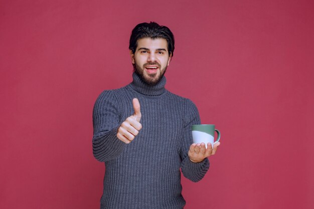 Homme en pull gris tenant une tasse de café et appréciant le goût.