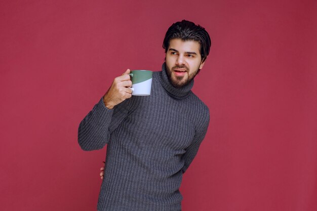 Homme en pull gris tenant une tasse de café dans la main.