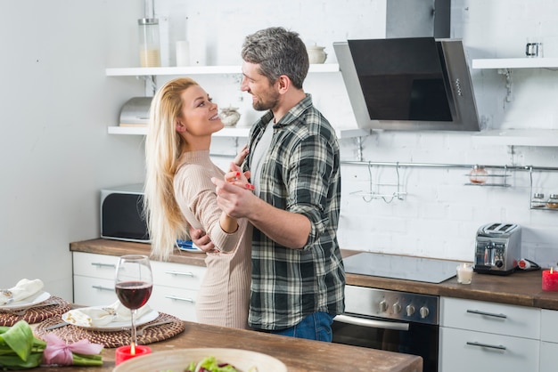 Homme qui danse avec une femme souriante près d&#39;une table dans la cuisine