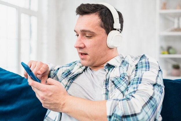 Photo gratuite homme qui écoute de la musique au casque et navigant sur un smartphone sur un canapé