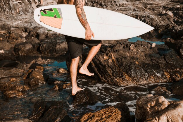 Homme qui marche sur la plage de galets avec planche de surf près de l&#39;eau