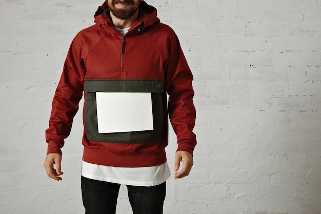 Un homme qui rit dans un élégant anorak rouge et gris avec une feuille de papier blanc uni sur sa grande poche avant sur blanc