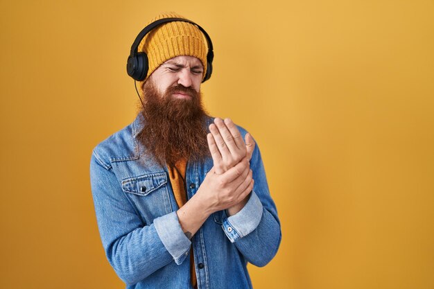 Homme de race blanche avec une longue barbe écoutant de la musique à l'aide d'un casque souffrant de douleurs aux mains et aux doigts inflammation de l'arthrite