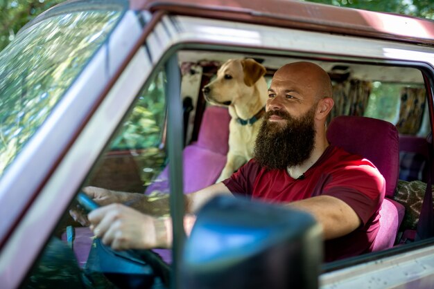 Homme de race blanche monté sur sa voiture avec son Golden Retriever