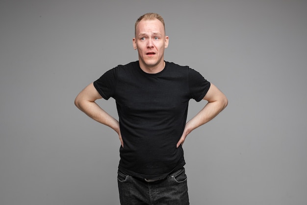 Homme de race blanche portant un t-shirt noir et un jean posant avec les mains sur une ceinture isolée sur un mur gris