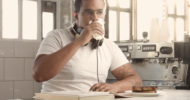 Homme de race mixte dessinant dans un loft ensoleillé écoutant de la musique dans des images d'écouteurs avec des touches ensoleillées