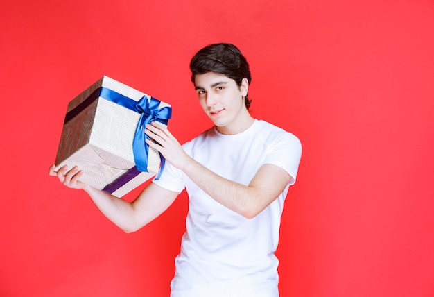 Homme recevant et tenant une boîte cadeau blanche enveloppée de ruban bleu avec les deux mains