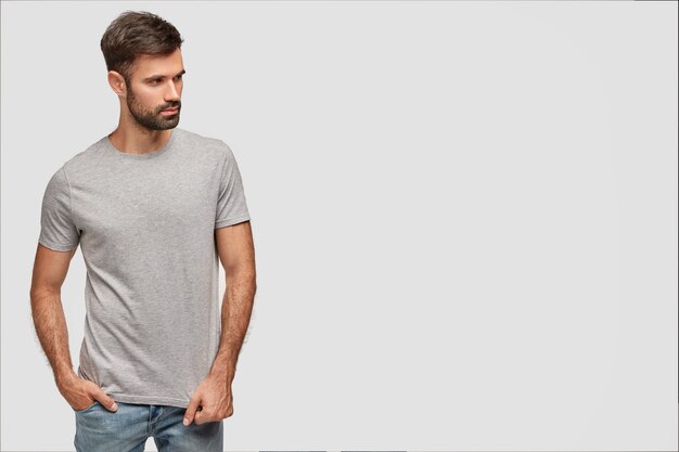 Homme réfléchi fort en t-shirt et jeans, annonce des vêtements à la mode de boutique, garde la main dans la poche