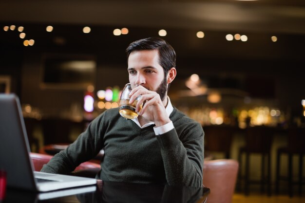 Homme regardant un ordinateur portable tout en ayant un verre de boisson