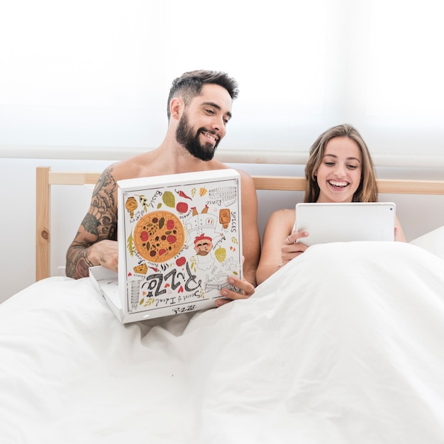Photo gratuite homme regardant sa femme à l'aide d'une tablette numérique en mangeant une pizza