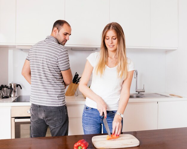 Homme regardant sa femme couper la carotte fraîche avec un couteau dans la cuisine