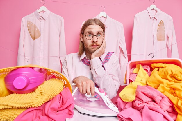 l'homme repasse la lessive a beaucoup de travail sur la maison a confus l'expression du visage porte des lunettes rondes chemise et cravate autour du cou