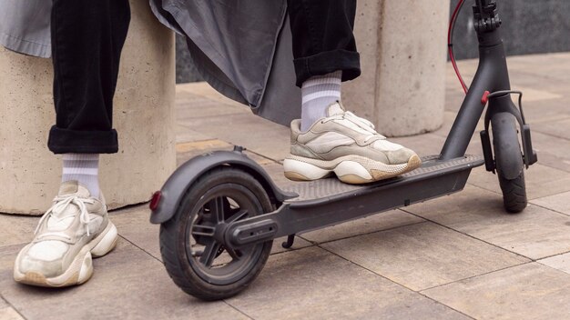 Homme reposant son pied sur un scooter électrique à l'extérieur