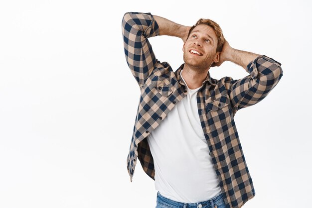 Homme rêveur rousse se reposant tenant les mains derrière la tête et regardant le coin supérieur gauche avec un sourire rêveur rêvassant regardant la publicité debout sur fond blanc