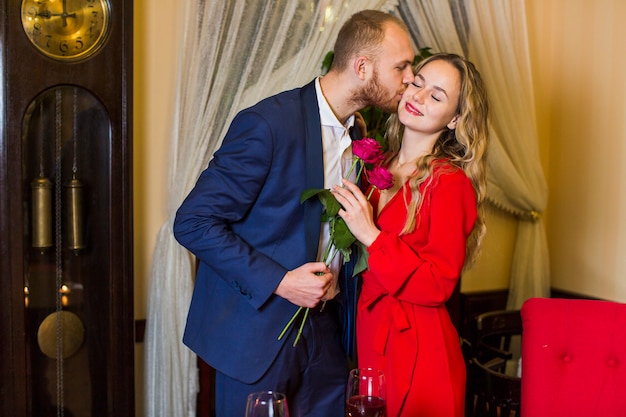 Homme avec des roses, embrassant une femme sur la joue au restaurant