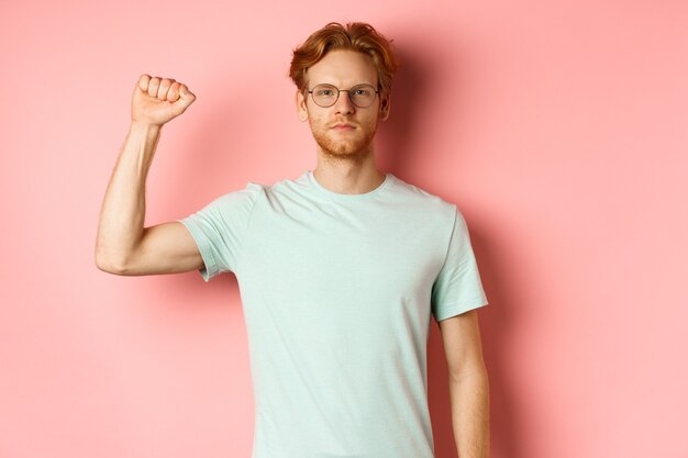 Homme rousse confiant debout uni à la vie noire importe movemet, montrant le poing levé et regardant sérieusement la caméra, protestant et étant un activiste, debout sur fond rose.