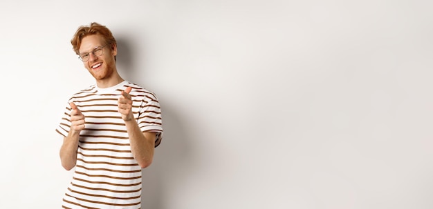 Photo gratuite homme rousse cool et impertinent avec barbe et lunettes pointant des pistolets du doigt à la caméra et cong souriant