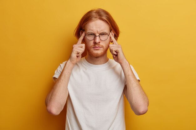 Un homme rousse en détresse presse les doigts sur les tempes, a une expression de visage impuissante