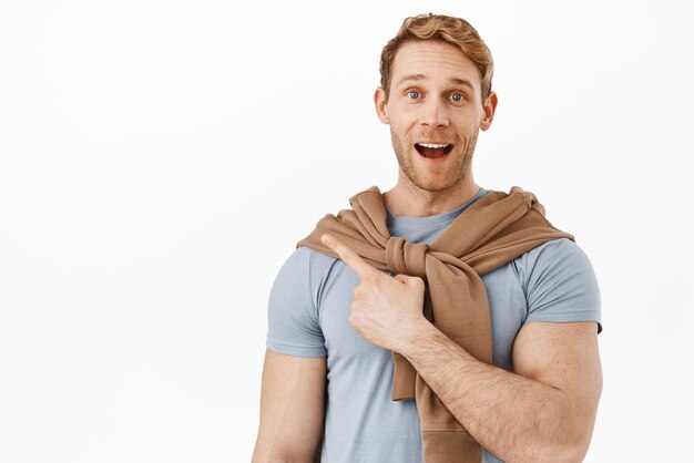 Homme rousse heureux et excité souriant pointant vers le coin supérieur gauche avec un visage impressionné et heureux regarde ce que j'ai trouvé geste montrant la publicité du produit fond blanc