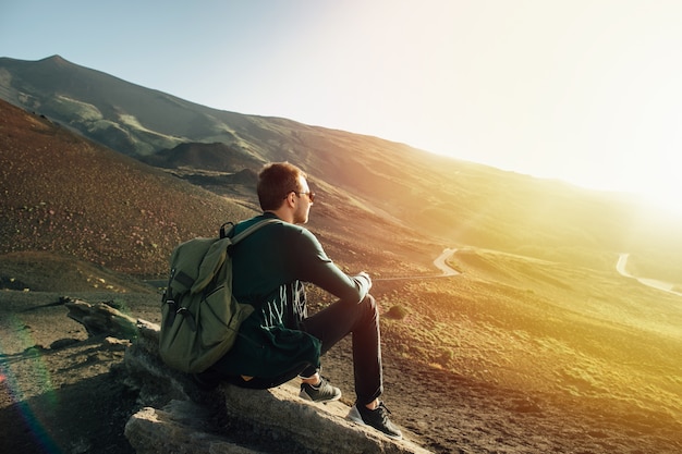 Homme avec sac à dos assis sur le rocher au coucher du soleil sur le volcan Etna montagne en Sicile