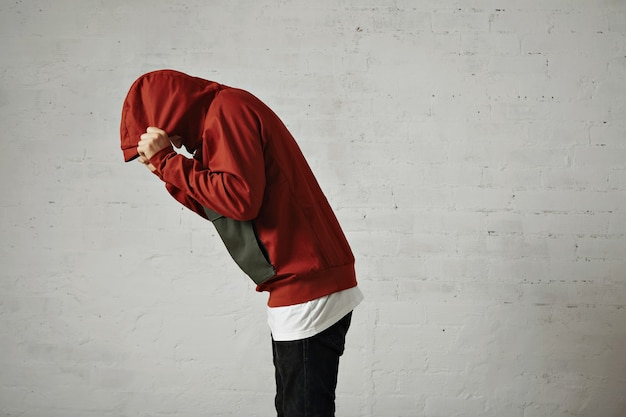 Photo gratuite un homme se penche et se couvre la tête avec la capuche de sa parka rouge, portrait de côté, sur blanc