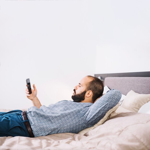 Homme se prélasser avec un smartphone sur le lit