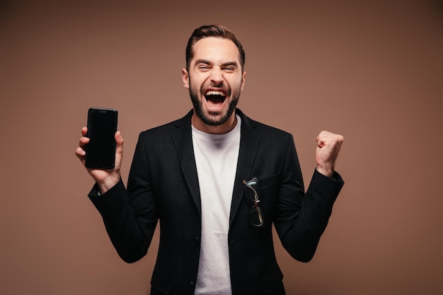 L'homme se réjouit et pose avec un smartphone sur fond marron